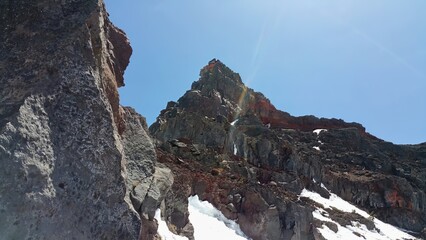 Low angle view of a rocky mountain peak with patches of snow under a clear blue sky on a sunny day