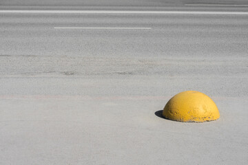 Yellow traffic curb stop positioned on a gray road in daytime near a busy street