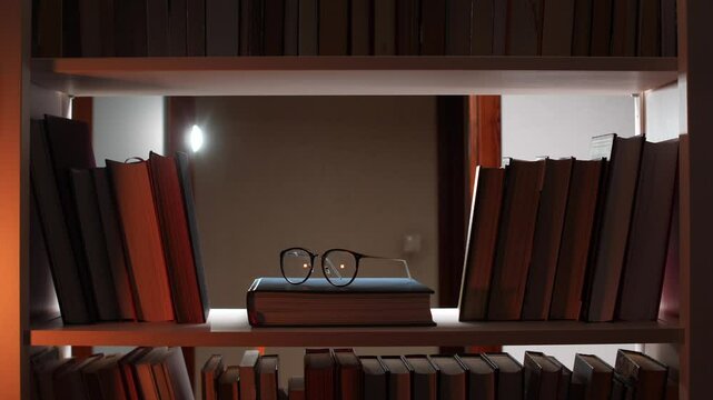 Eyeglasses resting on book in illuminated bookshelf