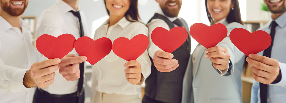 Group of joyful business people holding red hearts in a row, close-up. Friendly relations in a successful team. Concept heart shape, effective communication, gratitude, employee engagement