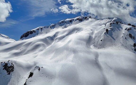 An aerial view of a snow covered mountain range under a blue sky with scattered white clouds above it - Powered by Adobe