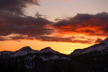 Sunset over snowy mountain peaks with orange and gray clouds filling the sky at dusk in a scenic view