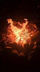 A vibrant campfire burns brightly in the darkness surrounded by rocks and scattered branches around it