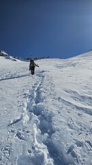 A person hiking uphill through a snowy mountain landscape under a clear blue sky on a bright day