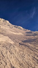 A snowy mountain slope under a clear blue sky showcasing textures and patterns of snow and ice formations