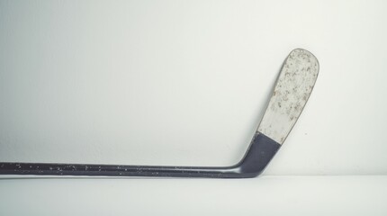 A hockey stick leaning on a white wall, close-up, soft shadows highlighting the stick and wall texture.

