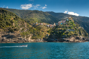 colorful buildings on a cliff between terraced hills, Monterosso al Mare, Cinque Terre, boat on the blue waters of the Ligurian Sea.