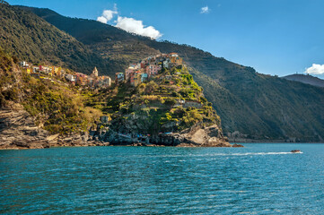 the cluster of colorful houses on the cliffs and terraced hills of Monterosso al Mare, Cinque Terre, a boat on the blue waters of the Mediterranean Sea.