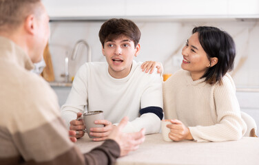 Happy family chatting and drinking tea together in the home kitchen