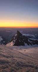 Snowy mountain peak at sunset with orange and blue sky and distant mountain range view from above