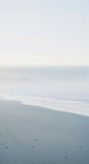 Serene Foggy Beach with Gentle Waves and Footprints

