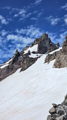A view of a rocky mountain peak covered in snow under a blue sky with scattered white clouds above it
