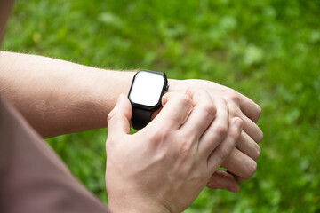 Close up man hands checking apps with smartwatch at nature green background. Male checking pulse,...