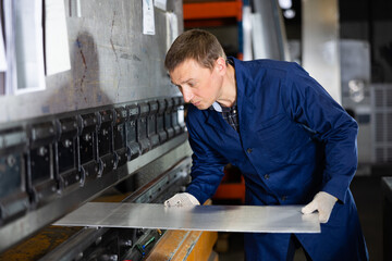 Metallurgical plant - male worker bending sheet of metal on a press