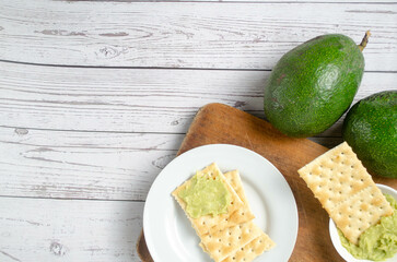 Avocado Dip with Crackers on Rustic Wooden Surface – Healthy Snack Concept. Avocado Dip and Crackers on Wooden Table. Healthy Snack with Avocado and Salted Crackers