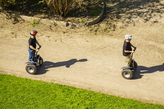 Two men wearing helmets ride Segways down the street