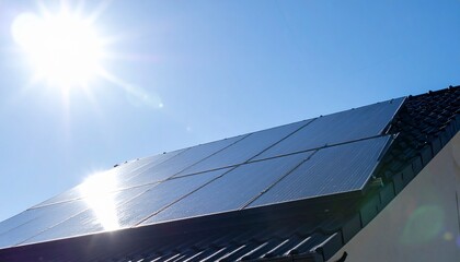 モダンな屋根の上に設置されたソーラーパネル群が輝く太陽に向かって角度を取り、透き通る青空を背景にレンズフレアが端に輝くクリーンで先進的なエネルギーシーン

