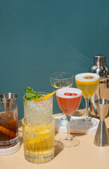 Colorful cocktails arranged on beige-green surface with bar tools