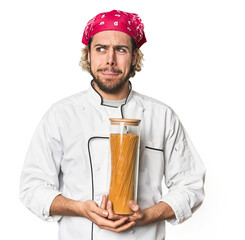 Young chef holds pasta sauce jar in studio confused, feels doubtful and unsure.