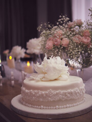 Elegant white celebration cake with delicate floral decoration, surrounded by soft tulle, candlelight, and fresh flower arrangements. Weding cake for bride