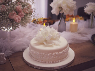 Elegant white celebration cake with delicate floral decoration, surrounded by soft tulle, candlelight, and fresh flower arrangements. Weding cake