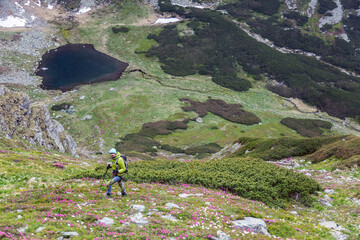 Adventure enthusiast hiking through dramatic rocky wilderness, using poles for stability while crossing steep terrain dotted with massive stones