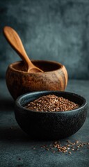 Dark bowl of flax seeds beside a wooden bowl and spoon against a moody backdrop