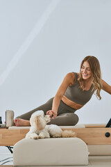 Happy smiling fit woman playing with her dog in sports outfit, ready for a pilates reformer trainig...