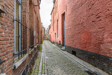 Narrow cobblestone alley between old brick residential buildings under cloudy sky at dusk in summer