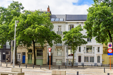 Town houses along a tree lined cobbled street in a city centre on a sunny summer day. One of the town houses has rooftop solar panels. 