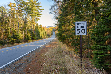 Speed limit sign along a deserted straight stetch of a forest road in the mountains at sunset in autumn