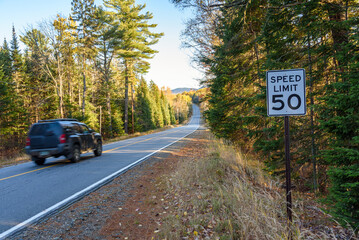 Car passing by a speed limit sign on a forest road in the mountains at sunset in autumn