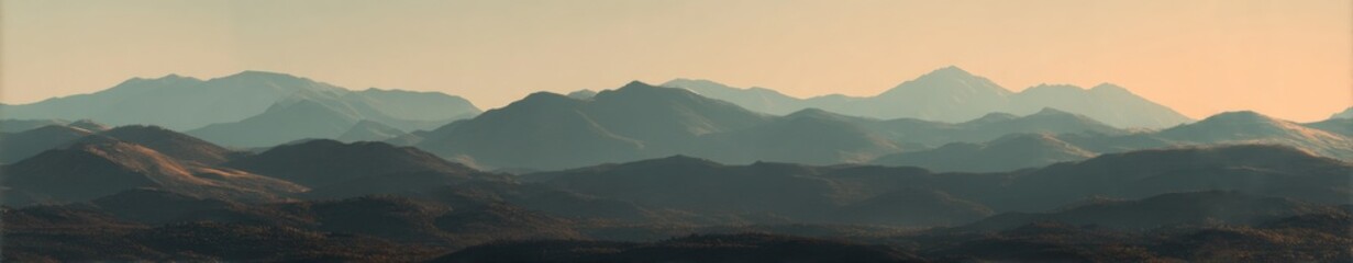Soft-focus panorama of a hazy mountain range at dawn or dusk, showing layers of muted blues and browns