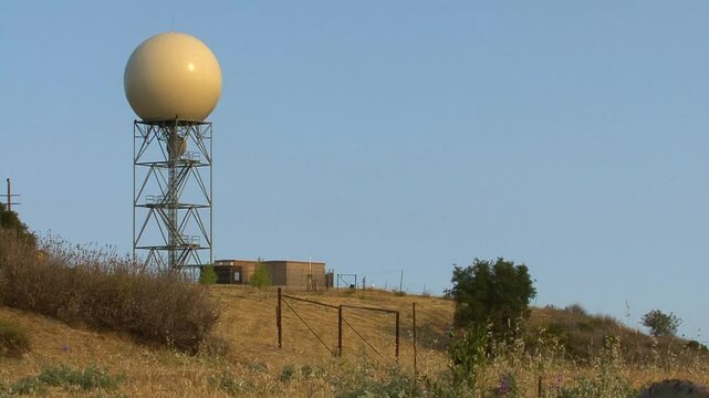 A doppler weather radar station, with a white dome on a metal tower, is sited in a dry grass field near the top of Sulpher Mountain in Ventura County, California. 