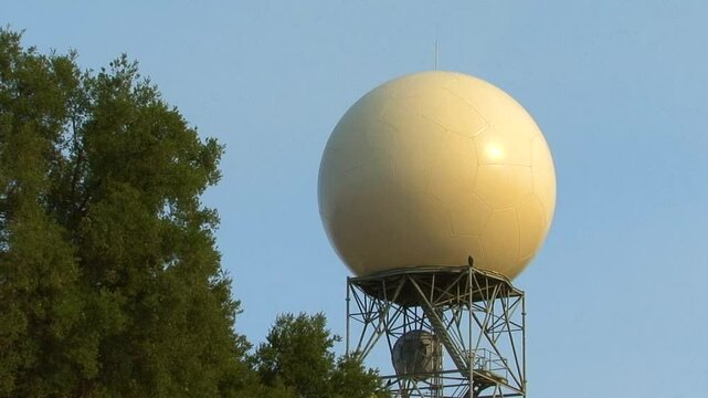 A doppler weather radar dome on a metal tower, sited in among pine trees near the top of Sulphur Mountain in Ventura County, California. 
