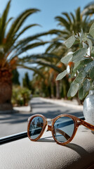 Brown sunglasses rest on a car dashboard, reflecting palm trees lining a sunlit road, evoking a sense of summer vacation and travel