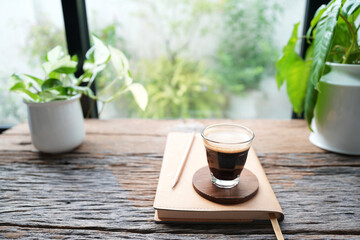 Coffee and brown small notebook on rustic wood table by the window