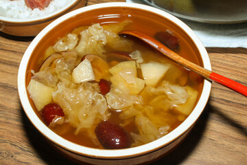  A close-up of a traditional Chinese dessert soup with white fungus, pear, and red dates in a ceramic bowl, with a spoon resting inside.