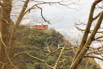 Casa de cor vermelha no topo da serra cercada por galho secos de árvores. 