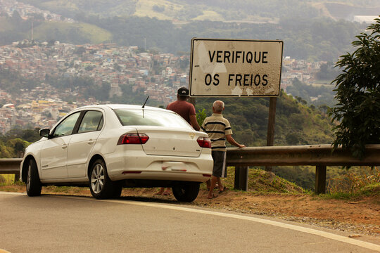 Carro de cor branca parado no acostamento de estrada no topo de uma decida. 