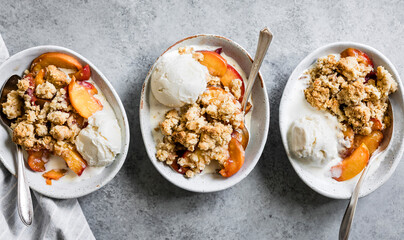 Three bowls of peach crumble with vanilla ice cream on a gray surface.