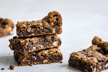 A stack of chocolate chip cookie bars with nuts on a light surface.