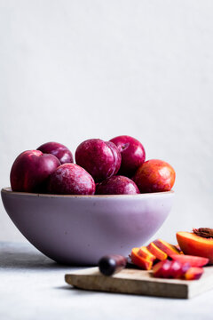 A bowl of fresh plums with sliced plums on a cutting board.