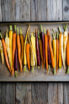 An assortment of colorful carrots arranged on a baking sheet with a rustic wooden background.