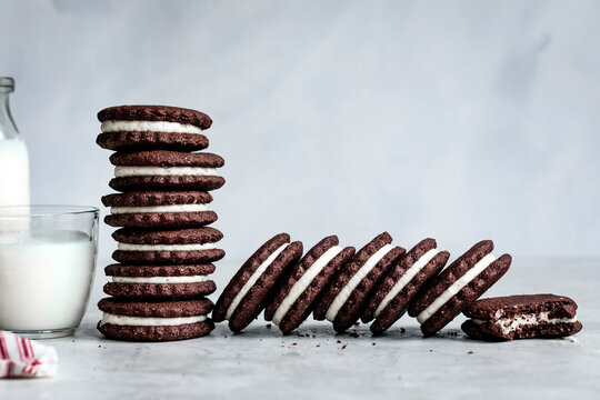 A stack of chocolate sandwich cookies with a glass and bottle of milk on a light background.