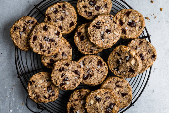 A batch of chocolate chunk cookies with nuts and sea salt on a cooling rack.