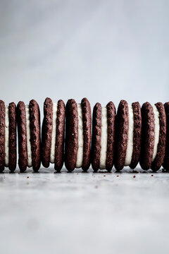 A row of chocolate sandwich cookies with white cream filling on a light surface.