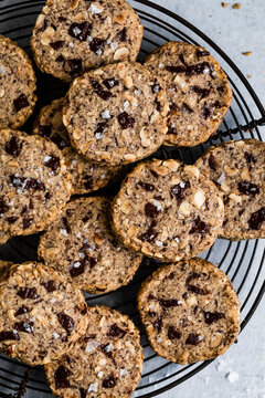 A batch of chocolate chunk cookies with nuts and sea salt on a cooling rack.