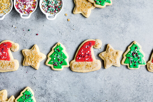 An assortment of Christmas-themed sugar cookies decorated with colorful icing and sprinkles on a gray surface.