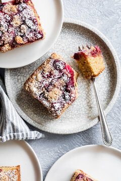 Top view of berry crumb cake slices on white plates with a fork and striped napkin.